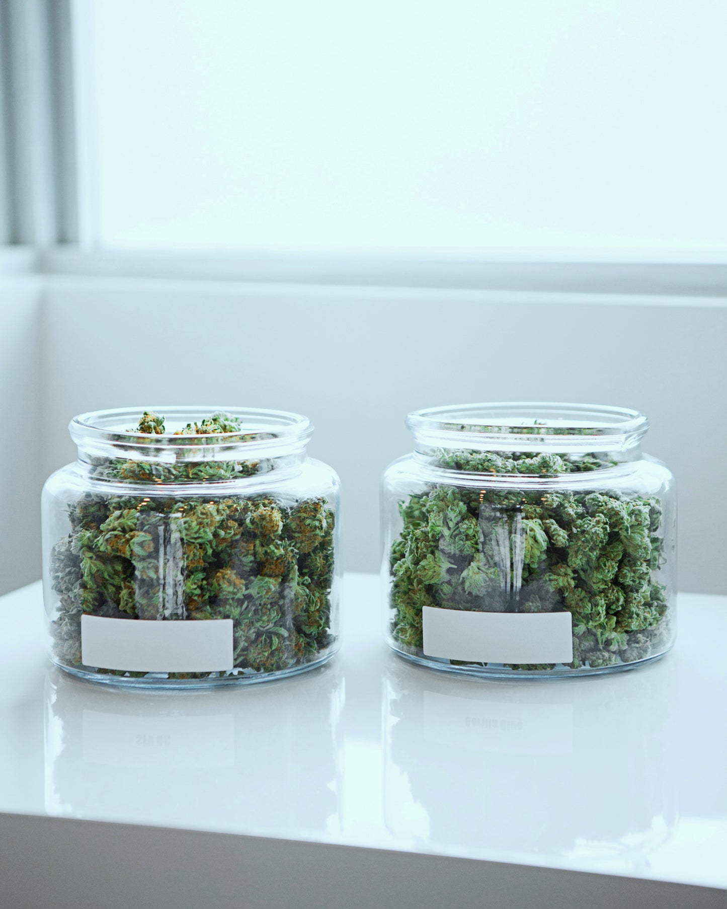 Two jars of cannabis on a white table.