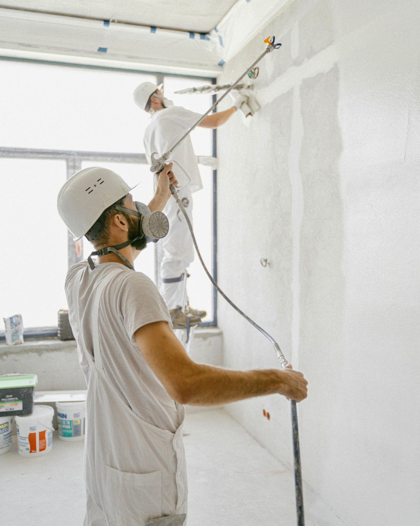 Two men painting a wall white.