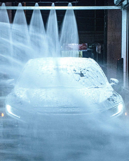 A soapy car being sprayed by water at the end of an automatic car wash.